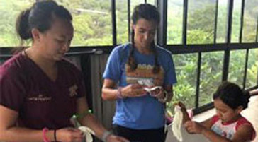 Three people at Smile Lodge prepare food together indoors with windows and greenery visible behind them.