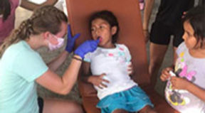 Healthcare worker administers vaccine to young child at community clinic, surrounded by parents and staff.