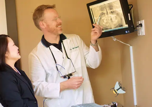 Dentist in white coat explaining X-ray to patient in clinical office setting.