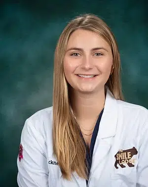 Professional portrait of a smiling woman in white medical coat against teal background at Smile Lodge.