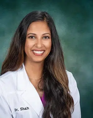 Professional headshot of Dr. Shah in white coat against teal background at Smile Lodge.
