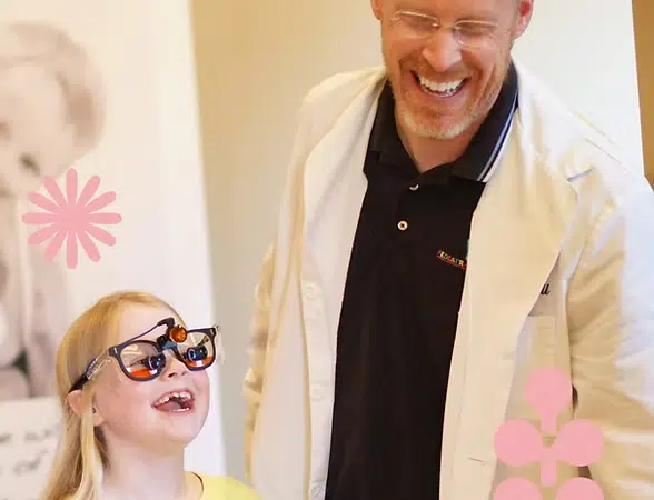 Adult and child smile together in bright dental office setting with pink flower decorations.