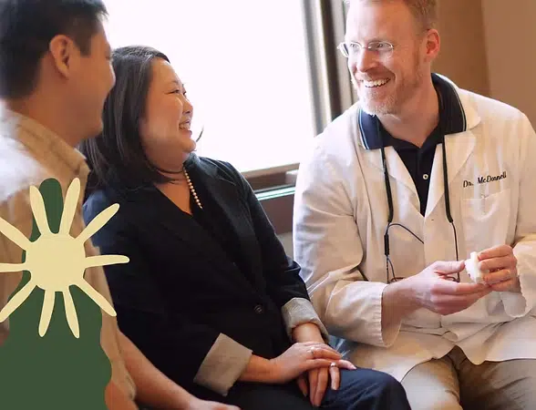 Doctor in white coat speaking with two patients in clinical consultation room at Smile Lodge.