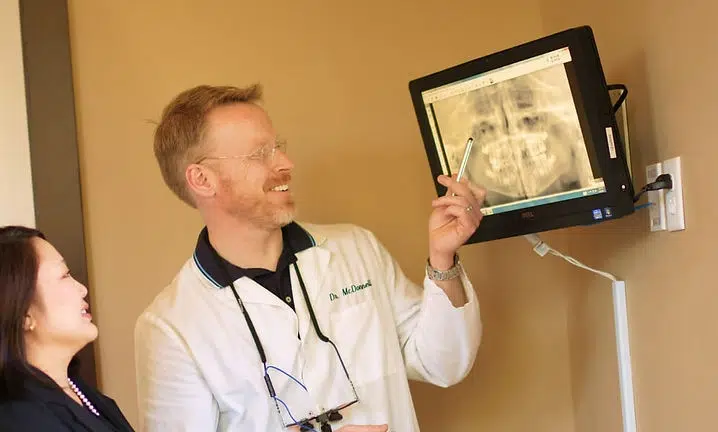 Doctor holding X-ray image while consulting with patient in medical office setting.