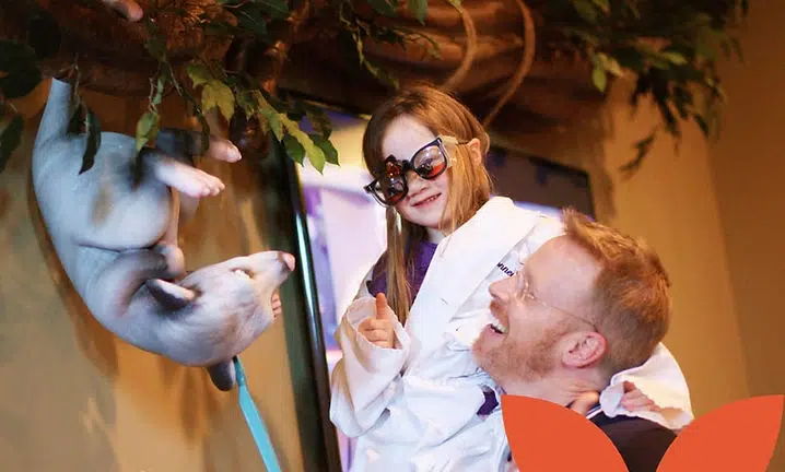Two people interact with a blue puppet character in an indoor theatrical setting at Smile Lodge.