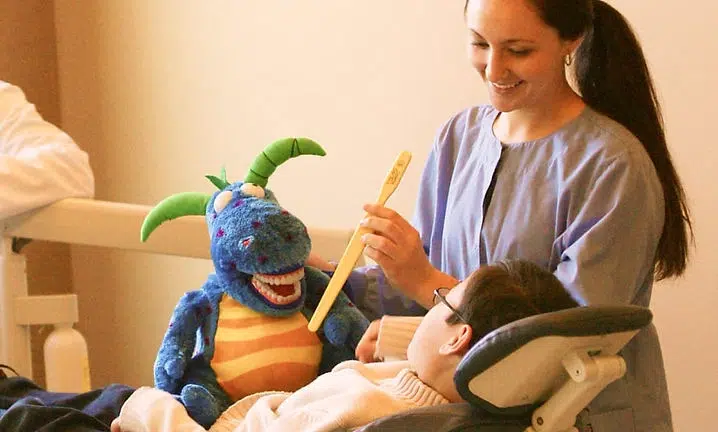 Woman playing with blue puppet toy on bed in cozy bedroom setting.