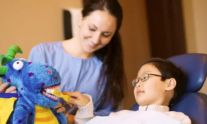 Woman and boy interact with blue puppet during therapy session indoors.