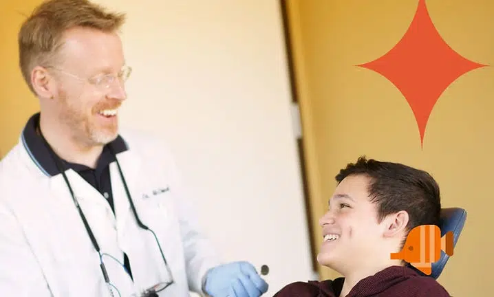 Healthcare provider in white coat smiling at young patient during medical visit at Smile Lodge clinic.