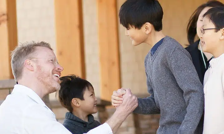 Adults and children greeting each other warmly indoors at The Smile Lodge community gathering.