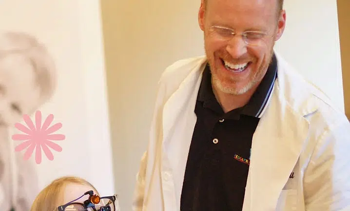 Adult man in cream cardigan smiling with young child in bright, welcoming indoor setting.