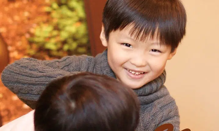 Two young children smiling and hugging indoors with warm autumn-colored background.