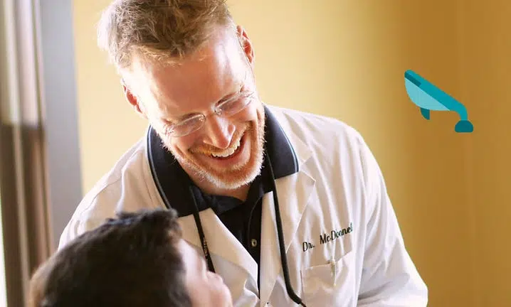 Doctor in white coat examines young patient with stethoscope in medical clinic setting.