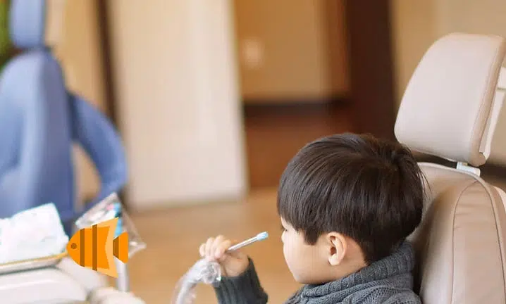 Young child sitting in car seat, reaching toward toy fish, indoor vehicle setting.