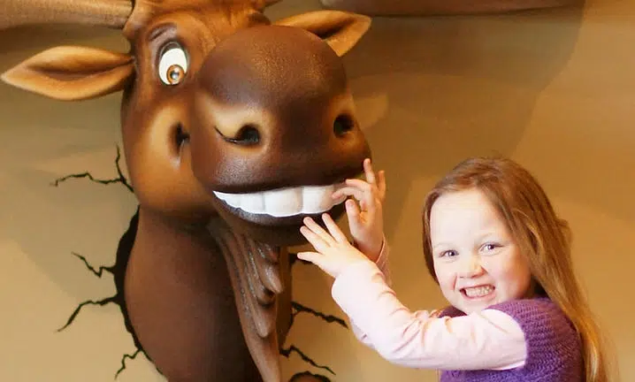 Young girl touching the smiling face of a large brown animal sculpture at the Smile Lodge.