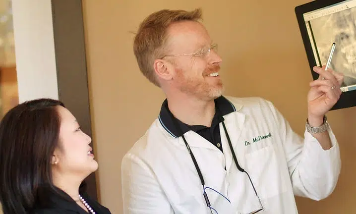 Male dentist showing dental X-ray to female patient in clinical office setting.