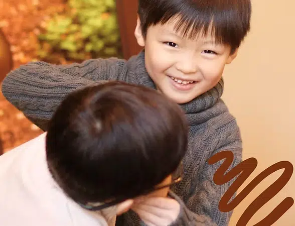 Young child hugging adult indoors, both smiling warmly at Smile Lodge facility.