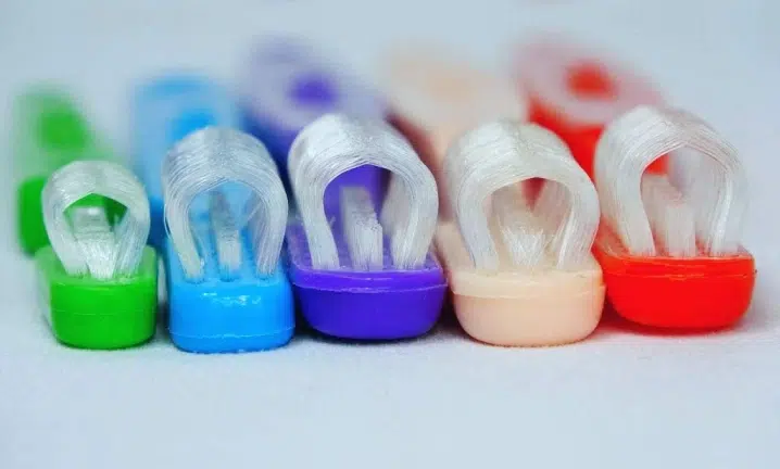 Five colorful toothbrush holders in green, blue, purple, beige, and red displaying white toothbrushes against neutral background.