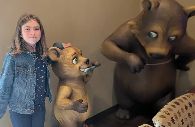 Young woman posing with two large bear statues in an indoor lodge setting.